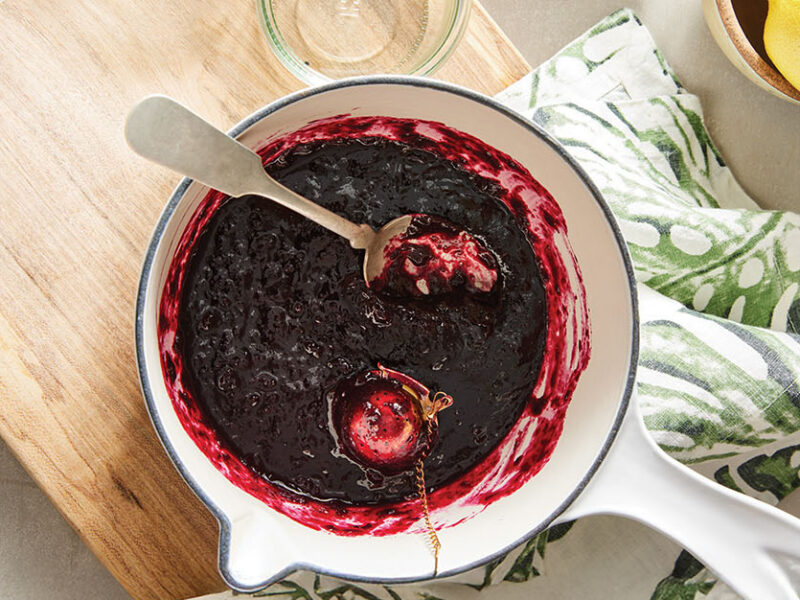 Looking down on a white pot of Small-Batch Blueberry Jam Without Pectin, with a spoon in the pot