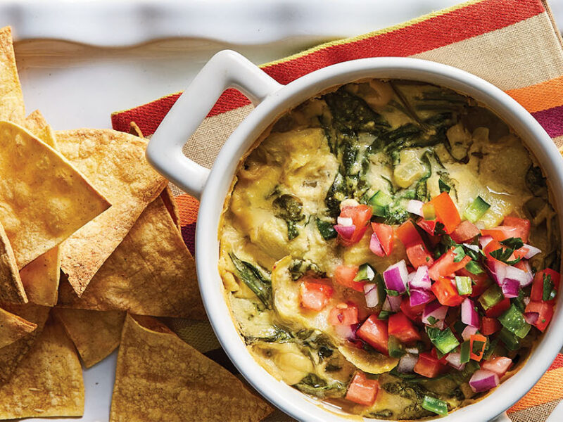 Cheesy Vegan Baked Spinach Dip on a white platter which a striped kitchen towel and backed tortilla chips
