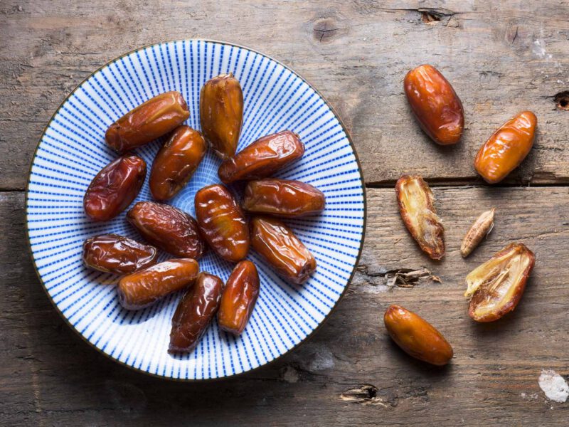 dates on a wooden table, some on a blue plate and some laid directly on the table and cut open