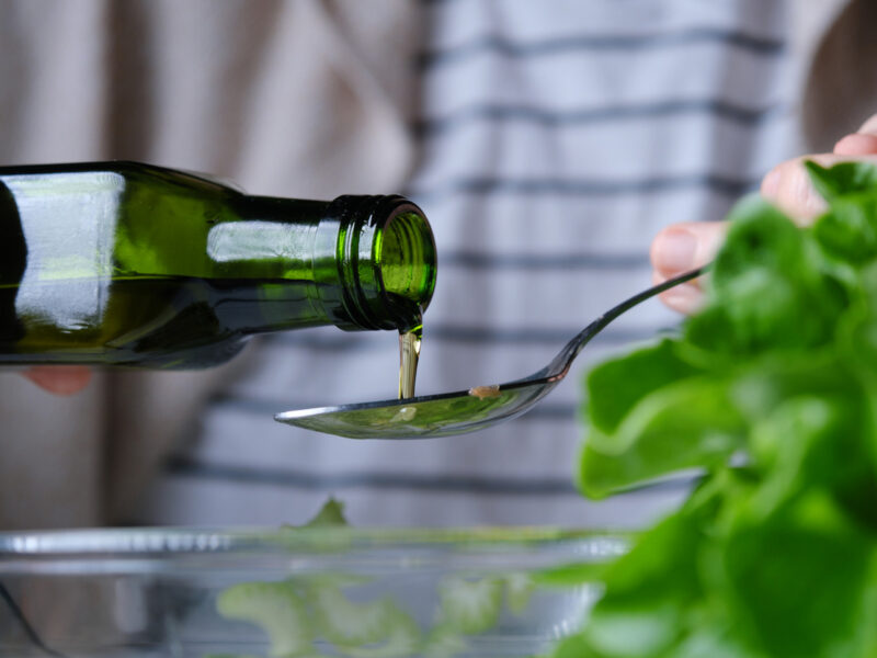 Someone pouring olive oil into a spoon over a bowl of salad
