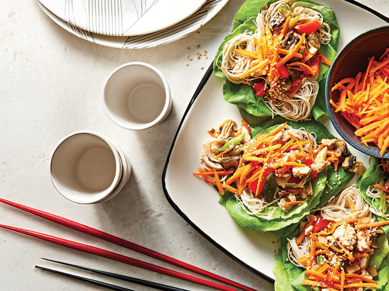 A square white plate of four Tofu Lettuce Wraps next to two sets of chopsticks.