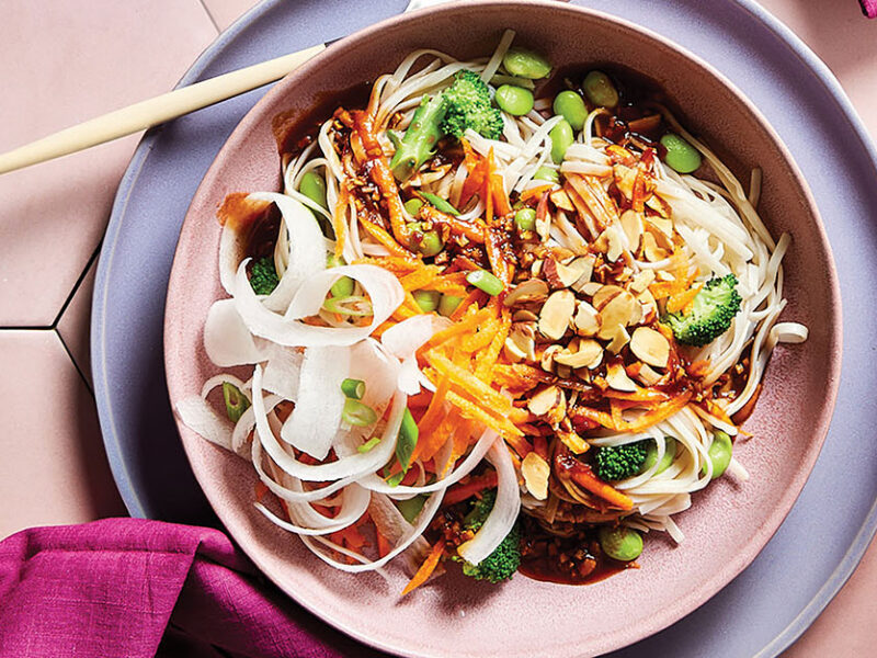 A wide-rimmed, pale pink bowl of 30-Minute Spring Roll Bowl with daikon ribbons and colorful veggies