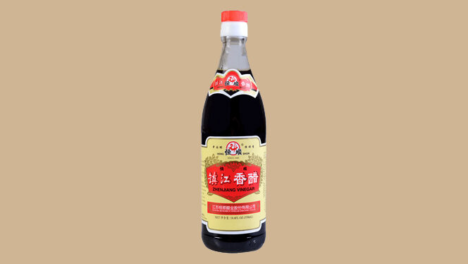 A bottle of Chinese black vinegar isolated on a tan background