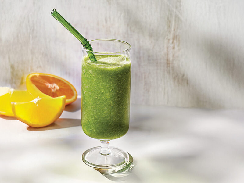 Kale Apple Smoothie in a wine glass with cut orange halves behind