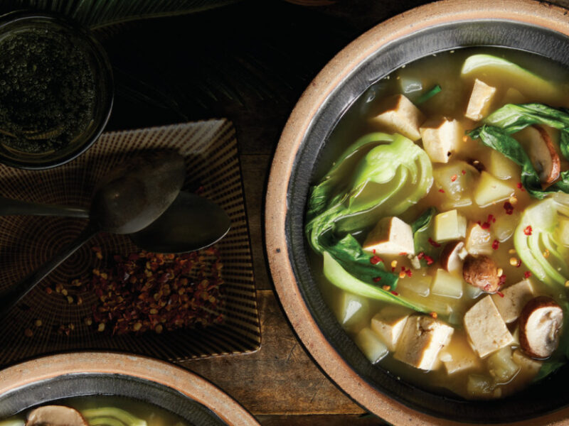 A brown ceramic bowl of Tinola against in a dimly lit setting