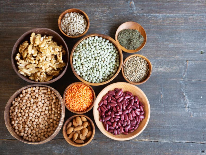 A collection of small and medium size bowls, each filled with legumes or nuts, on a wooden gray background
