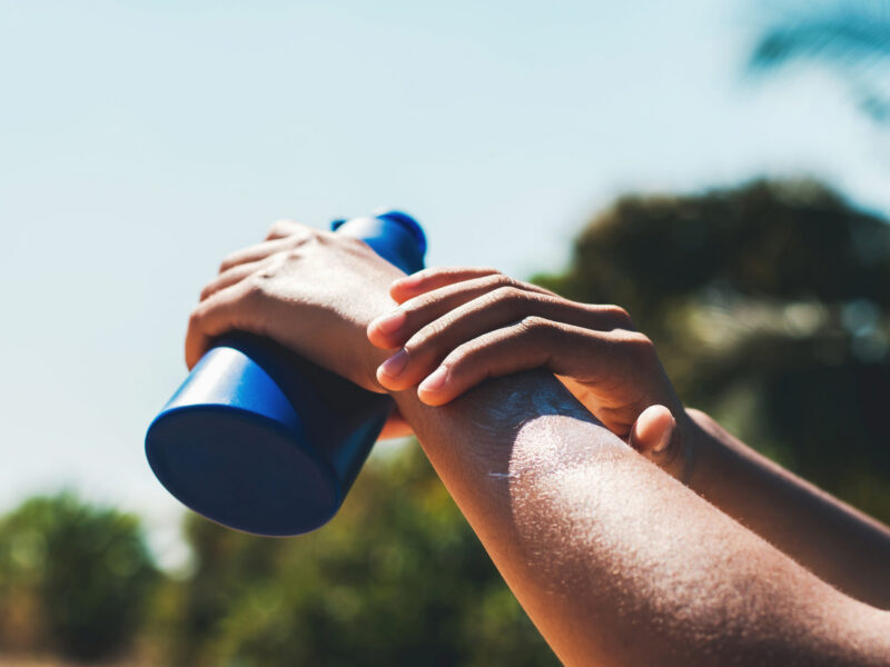 the arms of someone applying sunblock outside, holding the blue bottle of sunblock