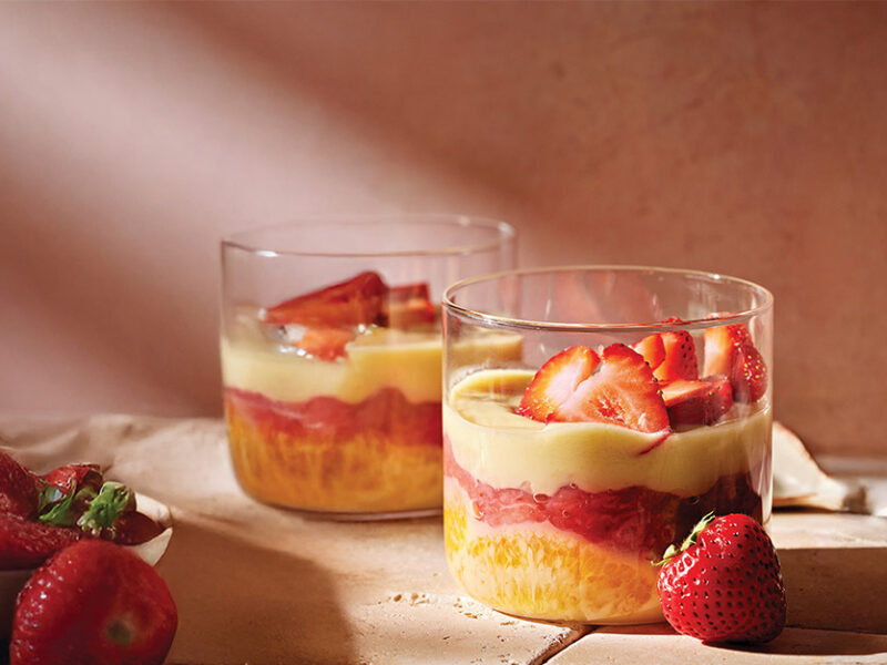 Two Strawberry-Orange Custard Cups in glass ramekins on a table with fresh strawberries and an orange