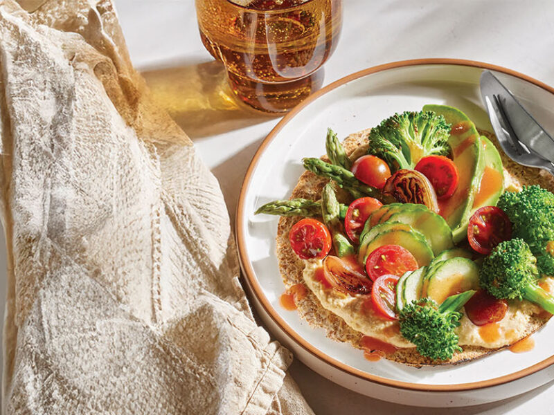 15-Minute Veggie Tostada on a plate drizzle with hot sauce next to a bowl of hummus