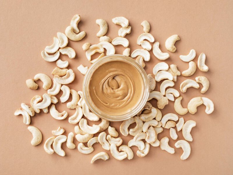 A jar of creamy cashew butter surrounded by raw cashews
