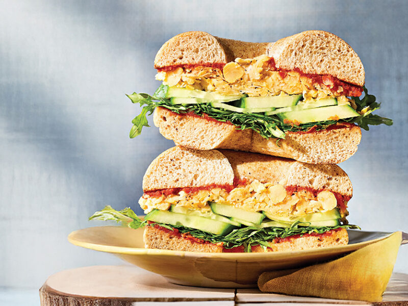A close-up of a Sun-Dried Tomato and Chickpea Bagel Sandwich cut in half and stacked on a plate