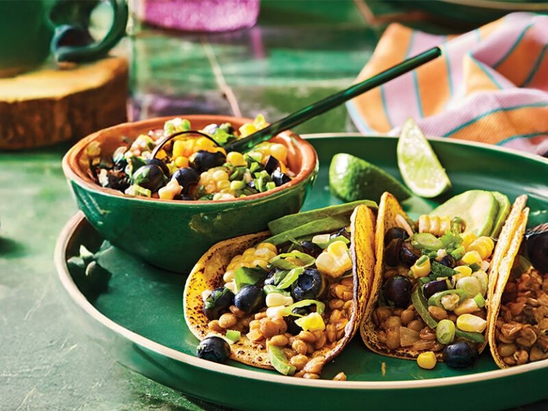 Three Lentil Tacos with Blueberry Corn Salsa on a green plate next to a small bowl of salsa