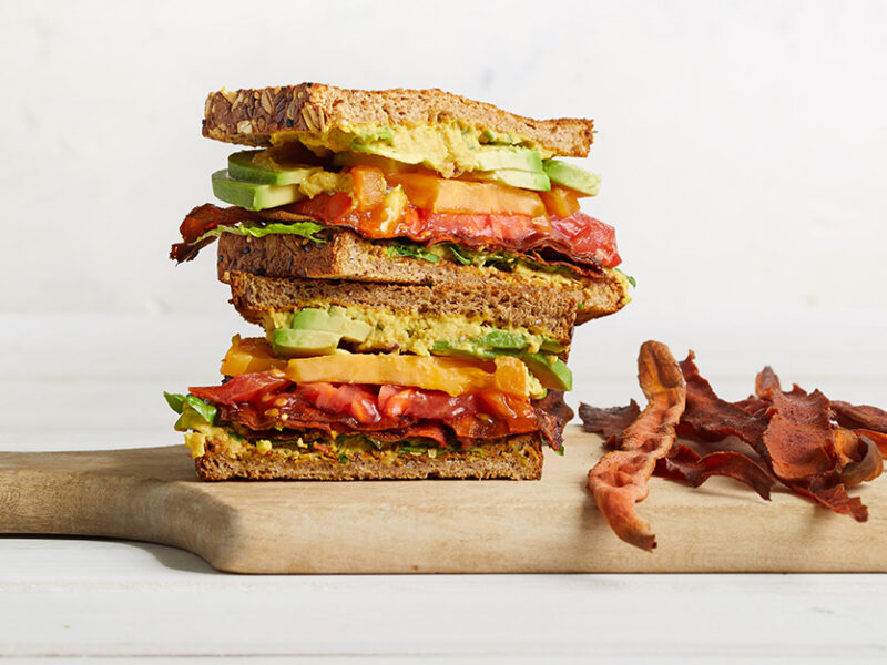 Vegan BLTA wit Carrot Bacon on a wooden chopping board against a white background