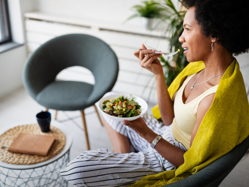 Woman sits back on a couch while eating a bowl with a healthy plant-based salad