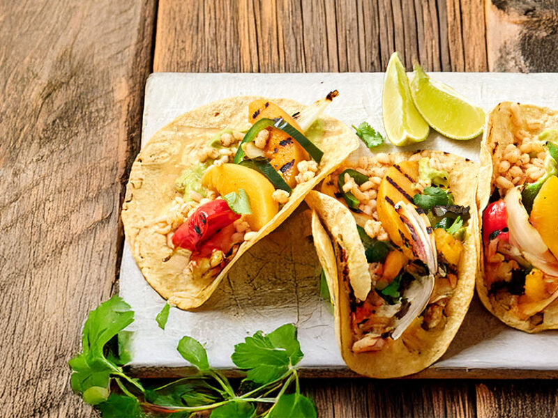 Four Peach and Pepper Tacos on a white board on a rustic wooden table