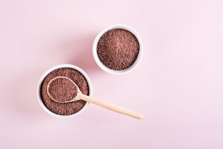 Kala namak (Black Himalayan salt) in bowl with wooden spoon on pale pink background