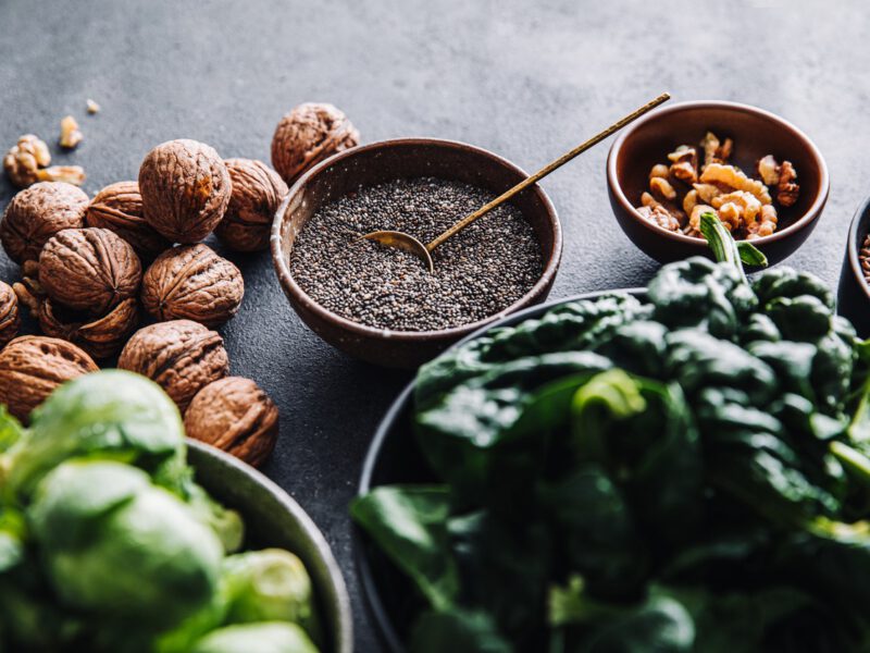 Close-up of omega 3 vegan food in bowls on black table: walnuts, chia seeds, nuts, and leafy greens