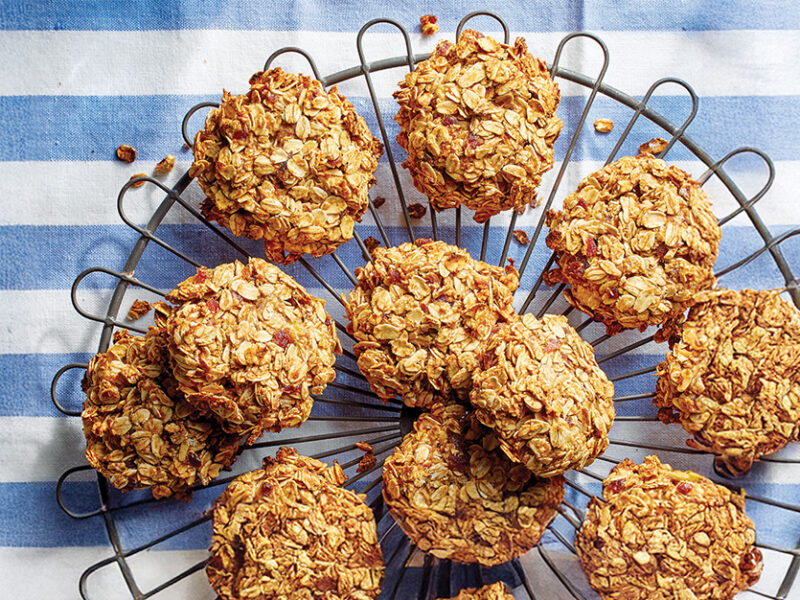 A cooling track piled high with Banana Oat Cookies, over a blue and white striped dish towel