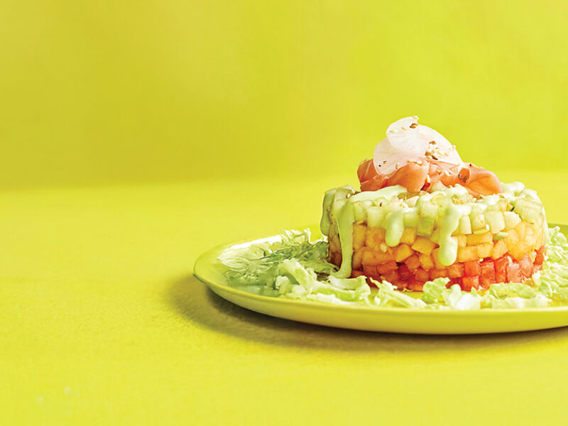 A plate with one Melon Poke Stack with Avocado-Wasabi Drizzle against a bright yellow-green background