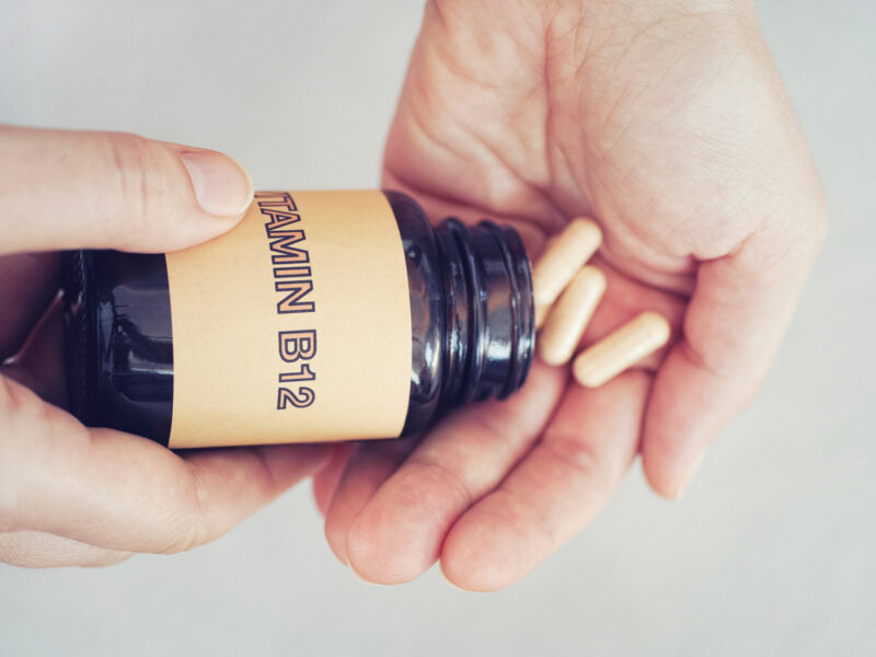 Hands pouring out a few vitamin b12 supplements from a plastic container