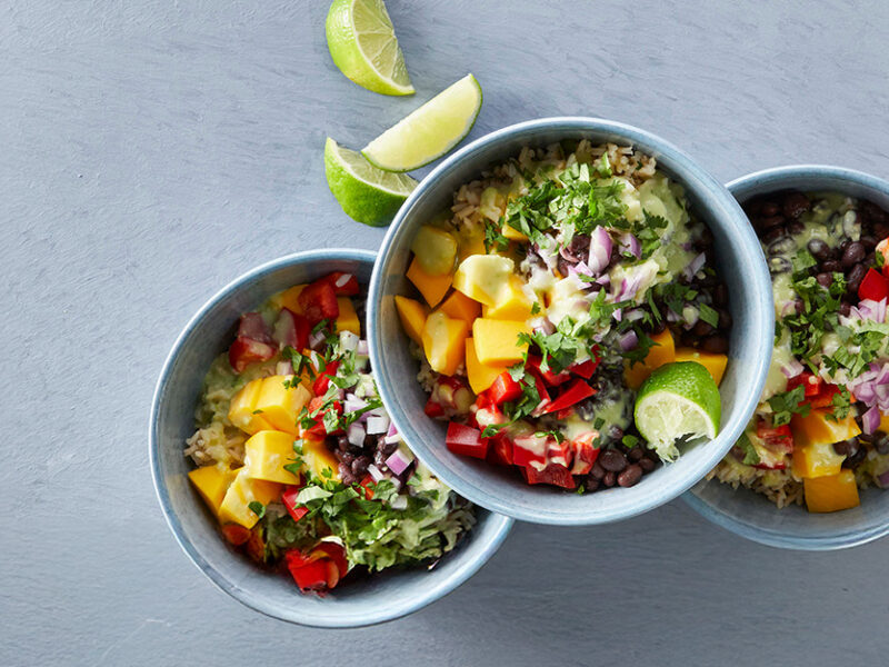 Two bowls of colorful Mango Rice Salad with a third on top, set against a grey background