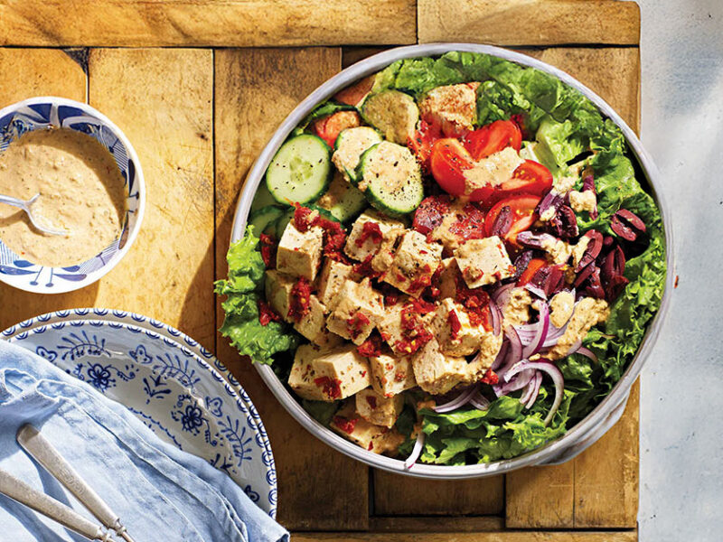 Greek Salad with Sun-Dried Tomato Tofu Feta in a serving bowl on a wooden chopping board