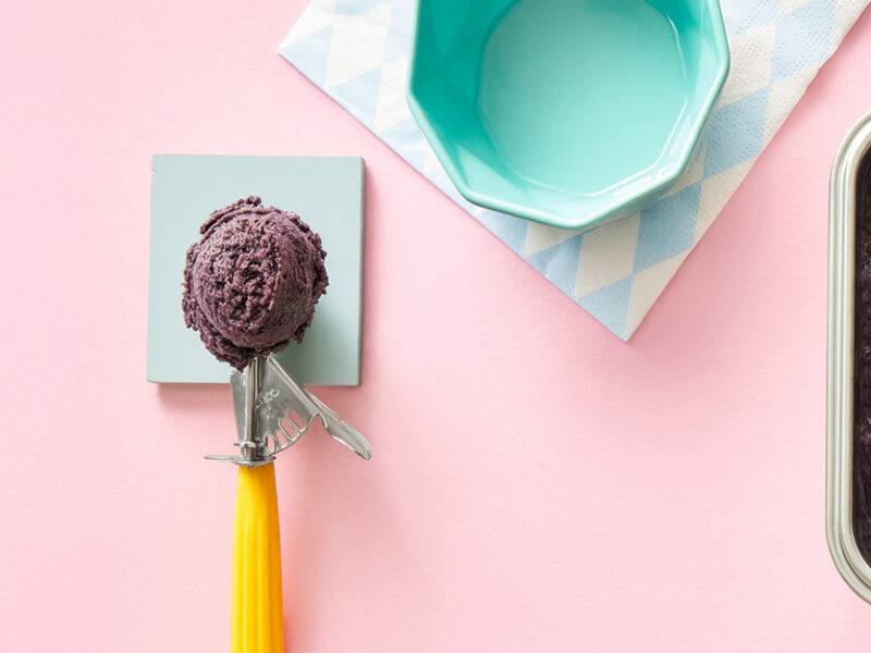 A scoop of Adzuki Bean Nice Cream next to a stainless steel container of the ice cream against a pale pink background