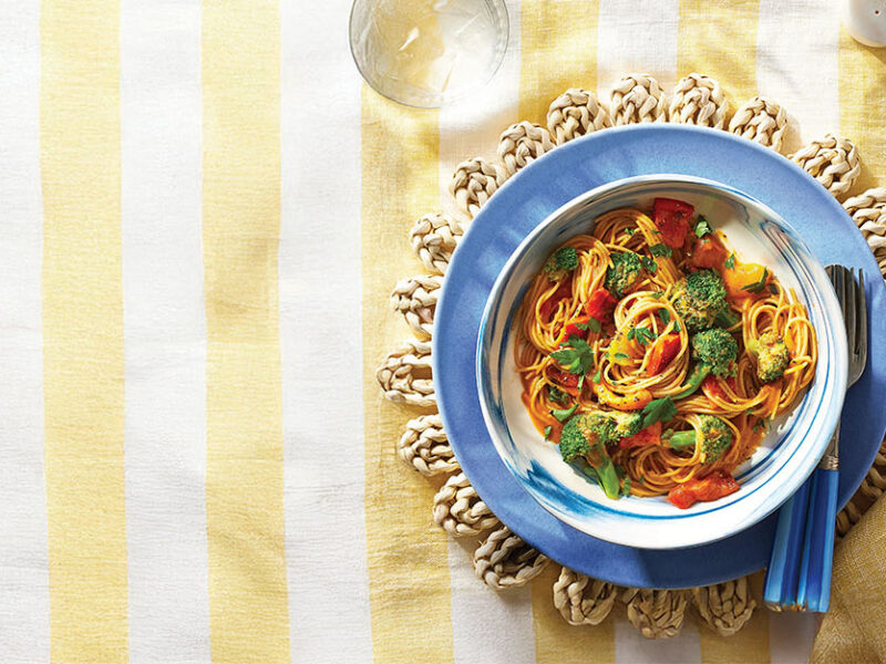 A blue ceramic bowl of Grilled Bell Pepper Pasta on a pale yellow and white tablecloth