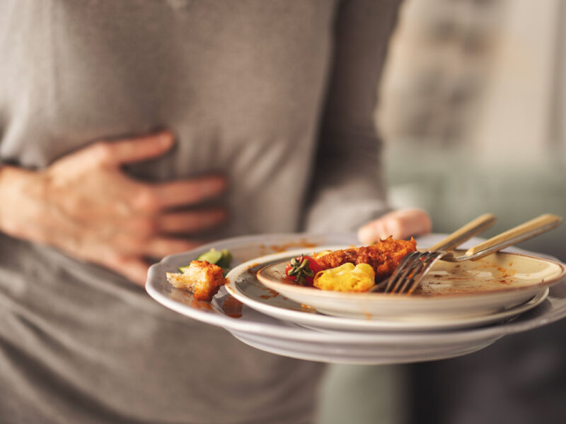 Person having heartburn and clutching their lower chest area with one hand while holding a plate of mostly eaten food in the other