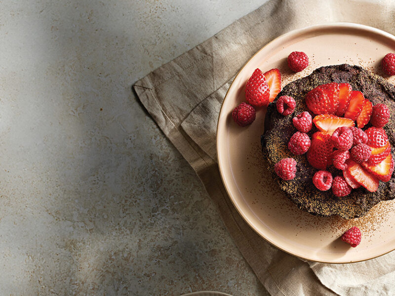 Slow-Cooker Chocolate Fudge Cake on a plate, topped with sliced strawberries and raspberries