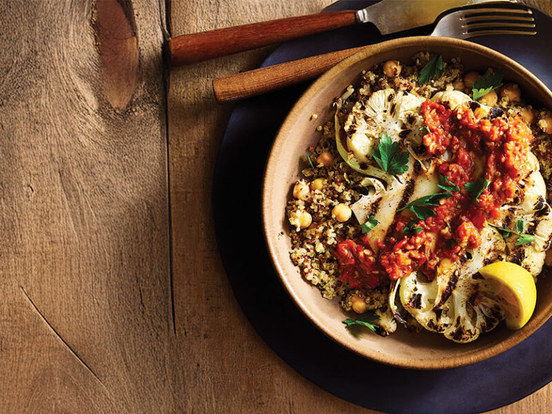 Grilled Cauliflower Steaks with Muhammara on an earthy brown plate on a dark wooden table top