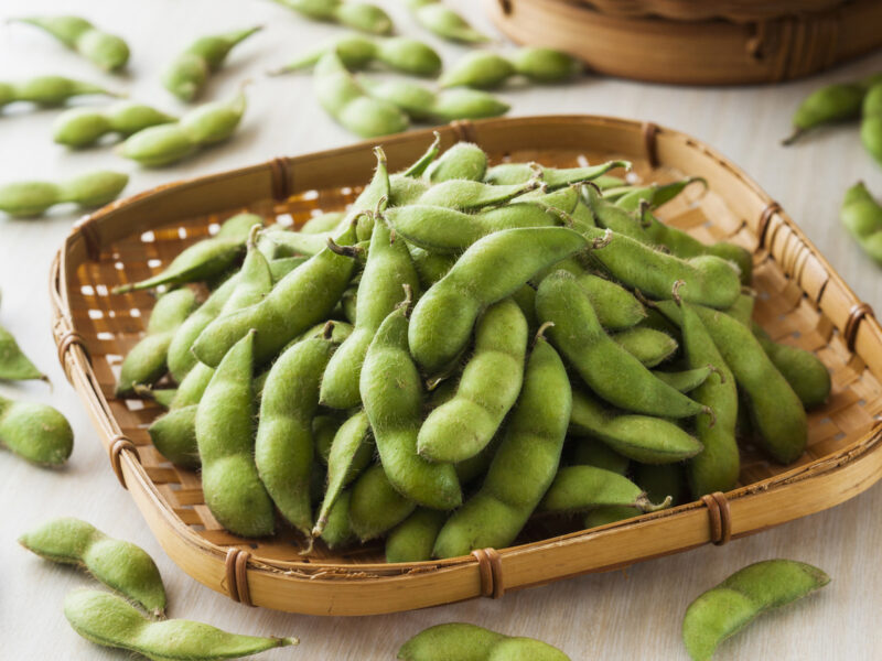 A pile of fresh or steamed edamame in a woven bamboo tray