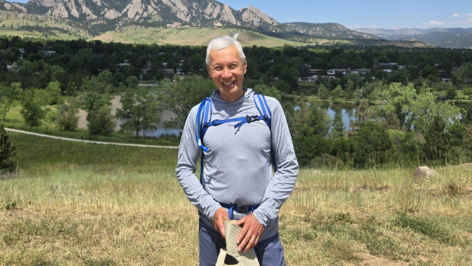 Jet Benitez wearing a backpack standing on a hill with a gorgeous vista behind him of a river and mountains