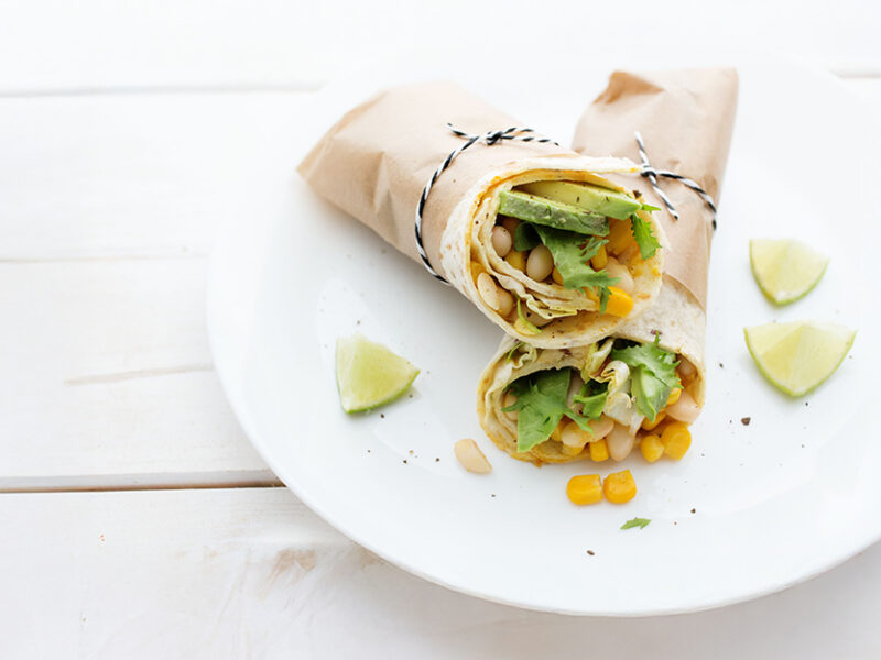 Two California Burritos on a white plate on a white table. The burritos are wrapped in paper and tied with a string.