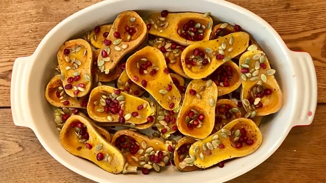 roasted honeynut squash in a casserole dish, sprinkled with pomegranate seeds and pepitas