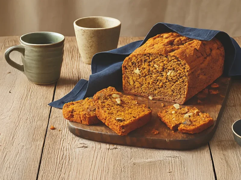 Pumpkin Spice Bread on a wooding chopping board, with a couple of slices cut, sitting in front of the loaf