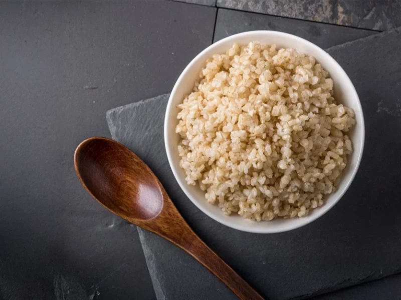 A bowl of Instant Pot Brown Rice against a dark grey background with a small wooden spoon beside the bowl