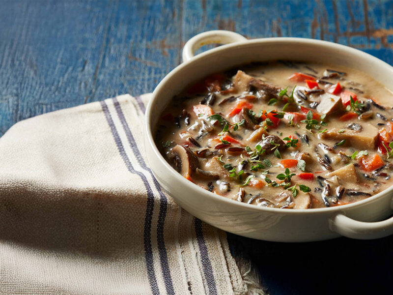 Creamy Wild Rice Soup in a wide-rimmed white bowl on a rustic blue wooden counter