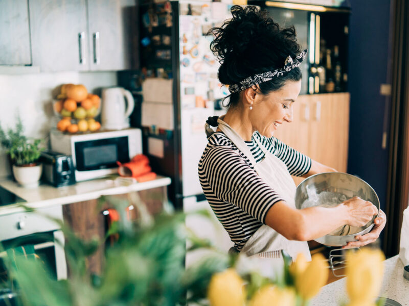 A bright image of a woman stirring batter in the kitchen, looking happy