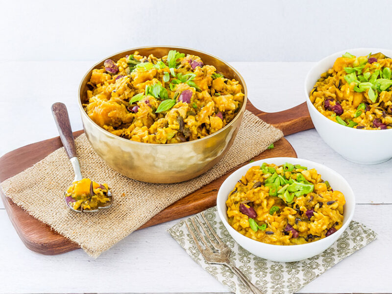 A large bowl of Caribbean Rice on a wooden chopping board next to two smaller bowls