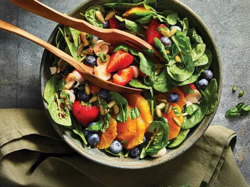 Sweet Spinach and Berry Salad in a green ceramic serving bowl with wooden tongs