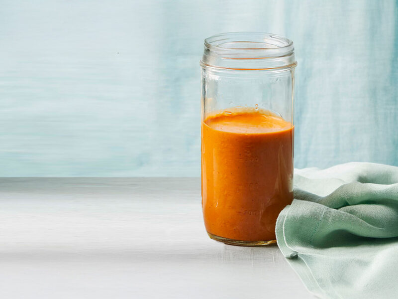 Vegan Queso Sauce in a glass jar, with a pale blue curtain in the backgroujd