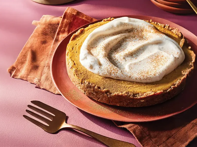 Vegan Pumpkin Cheesecake on a burnt orange plate, with a fork beside the plate and a large dollop of Aquafaba Whipped Cream on top.