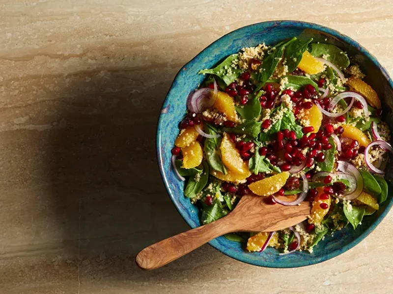 Date and Orange Couscous Salad in a blue ceramic bowl with a wooden spoon in the bowl