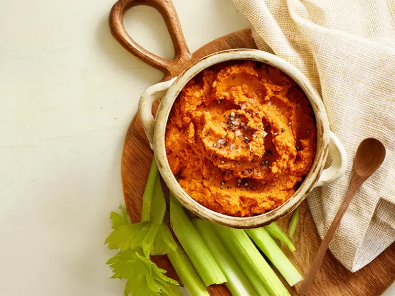 Harissa Hummus in a beige ceramic bowl on a chopping board with celery slices