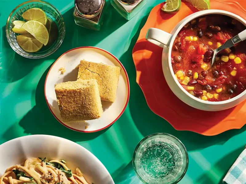 2-Bean Chili in a white bowl on a red plate, next to a small plate with two pieces of cornbread