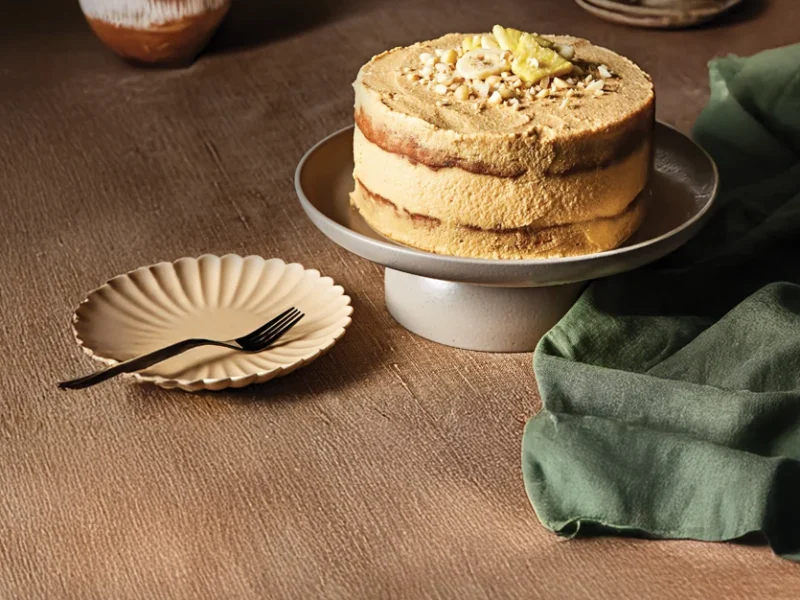 Banana Pineapple Cake with Macadamia Nuts on a cake stand with an empty plate and fork on the side