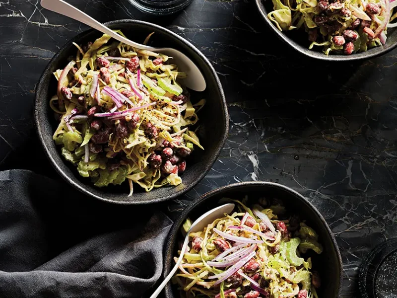 Three bowls of Easy Coleslaw with Red Beans and Rosemary. The bowls are black on a black backdrop so that the bright green and red of the coleslaw pops against the darker colors