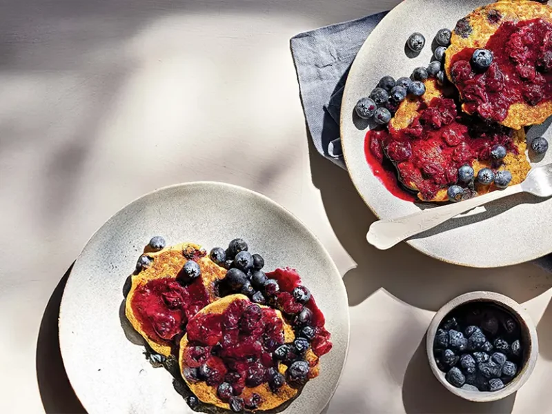 Two whites plates with Quinoa Pancakes drizzled with blueberry sauce