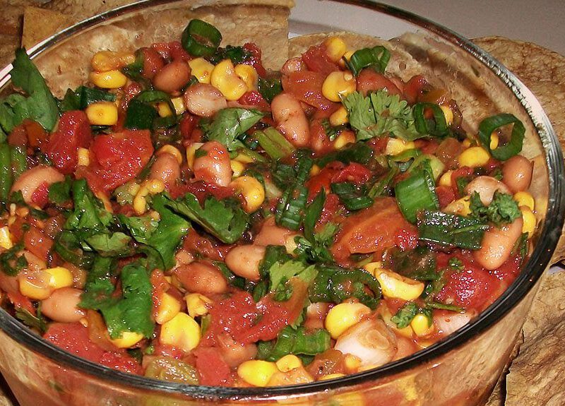 Chipotle Corn Salsa and Baked Tortilla Chips in a glass bowl with baked corn chips on a plate around the bowl